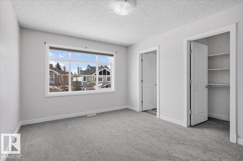 This room features neutral grey carpeting, light grey walls, and a window providing views of residential properties - 6 6410 134 Avenue Nw, Edmonton, AB - Indoor