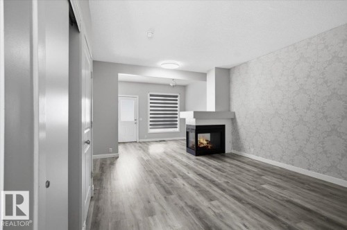 The property features wood-look flooring, a fireplace with a black surround, and a wall with patterned wallpaper - 6 6410 134 Avenue Nw, Edmonton, AB - Indoor With Fireplace
