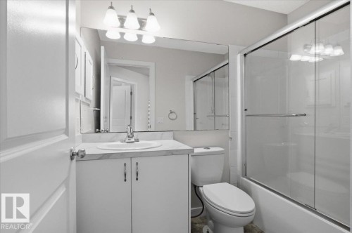 Bathroom featuring a vanity with a white countertop and cabinet storage, a toilet, and a bathtub with a glass sliding door - 6 6410 134 Avenue Nw, Edmonton, AB - Indoor Photo Showing Bathroom