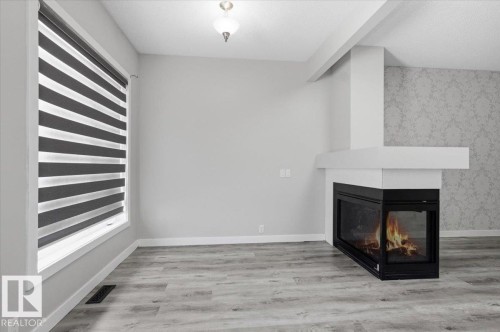 Living area featuring light-toned flooring, a corner fireplace with a white mantel, and a window with blinds - 6 6410 134 Avenue Nw, Edmonton, AB - Indoor With Fireplace