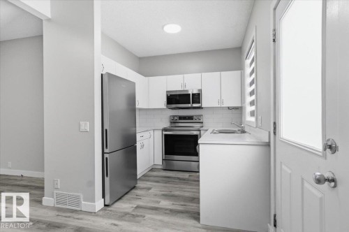 The kitchen features a stainless steel refrigerator, range, and microwave, complemented by white cabinetry, a subway tile backsplash, and a light-colored countertop - 6 6410 134 Avenue Nw, Edmonton, AB - Indoor Photo Showing Kitchen