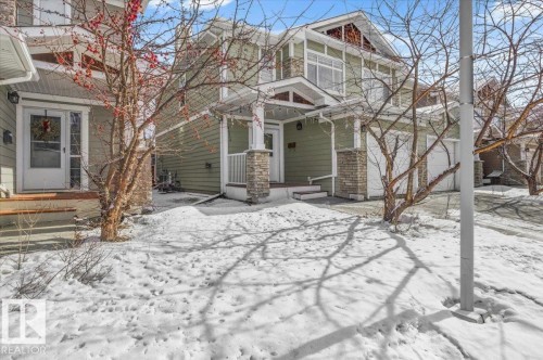 The property features light green siding, stone accents on the porch columns and garage, and a peaked roofline with decorative gable vents - 6 6410 134 Avenue Nw, Edmonton, AB - Outdoor With Facade