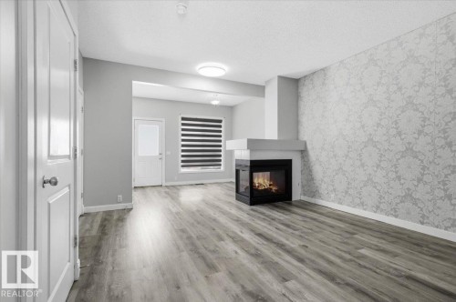 The living area features durable flooring, a modern fireplace, and a decorative accent wall - 6 6410 134 Avenue Nw, Edmonton, AB - Indoor With Fireplace