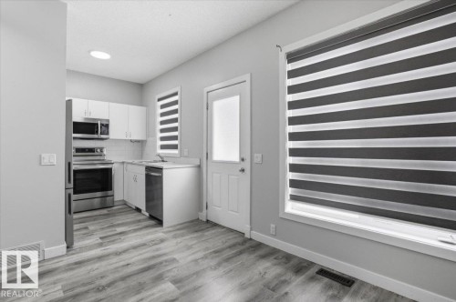 Kitchen and dining area featuring stainless steel appliances, white cabinetry, light countertops, and wood-look flooring - 6 6410 134 Avenue Nw, Edmonton, AB - Indoor