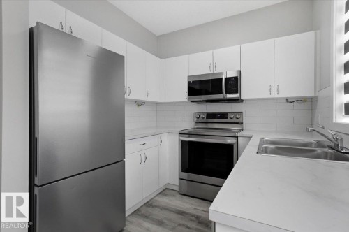 The kitchen features white cabinetry, stainless steel appliances including a refrigerator, oven, and microwave, and a double basin sink - 6 6410 134 Avenue Nw, Edmonton, AB - Indoor Photo Showing Kitchen With Double Sink