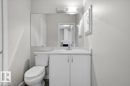 This bathroom features a vanity with a white countertop and a built-in sink, a toilet, and a mirror - 6 6410 134 Avenue Nw, Edmonton, AB - Indoor Photo Showing Bathroom