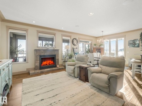 Living area with a premium fireplace, suspended lighting, plenty of natural light, and crown molding - 117 Mcdowell Wynd, Leduc, AB - Indoor Photo Showing Living Room With Fireplace