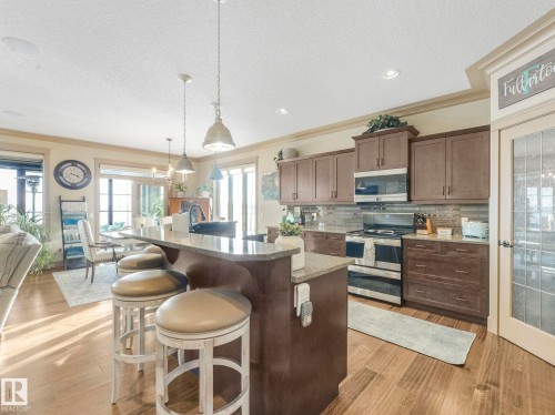 Kitchen with stainless steel appliances, crown molding, a kitchen bar, a textured ceiling, and light wood-type flooring - 117 Mcdowell Wynd, Leduc, AB - Indoor Photo Showing Kitchen With Upgraded Kitchen