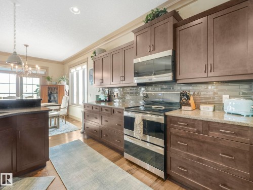 Kitchen featuring stainless steel appliances, ornamental molding, dark stone counters, light wood-style floors, and dark wood finish cabinetry - 117 Mcdowell Wynd, Leduc, AB - Indoor Photo Showing Kitchen