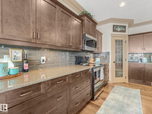 Kitchen featuring stainless steel appliances, decorative backsplash, a textured ceiling, light stone counters, and light wood finished floors - 117 Mcdowell Wynd, Leduc, AB - Indoor Photo Showing Kitchen