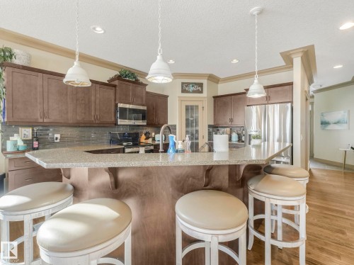 Kitchen featuring decorative backsplash, light stone counters, stainless steel appliances, a kitchen breakfast bar, and crown molding - 117 Mcdowell Wynd, Leduc, AB - Indoor Photo Showing Kitchen With Upgraded Kitchen