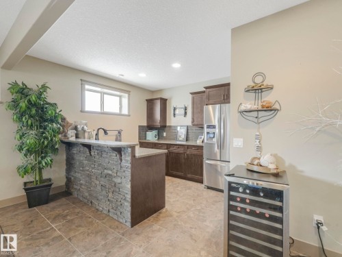 Kitchen featuring wine cooler, stainless steel fridge with ice dispenser, a breakfast bar area, a peninsula, and dark wood finish cabinetry - 117 Mcdowell Wynd, Leduc, AB - Indoor Photo Showing Kitchen