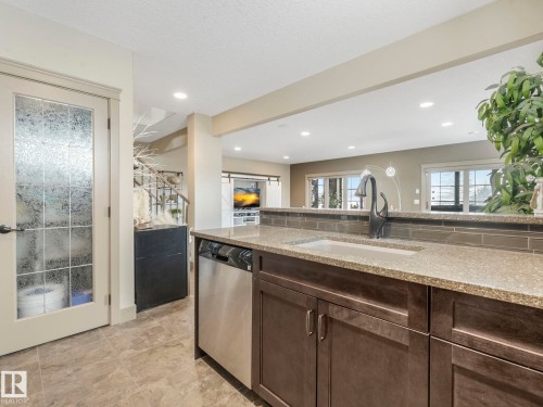 Kitchen featuring light stone counters, dark wood finish cabinets, stainless steel dishwasher, and recessed lighting - 117 Mcdowell Wynd, Leduc, AB - Indoor Photo Showing Kitchen