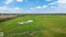 Expansive green landscape featuring open fields, scattered natural water features, and a distant tree line - 
