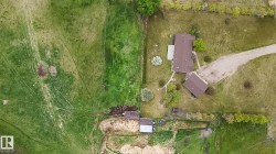 Spacious rural property featuring a primary residence with a brown shingle roof, a detached secondary structure, extensive green acreage, a gravel driveway, and mature perimeter trees - 