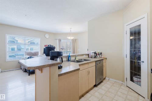 Kitchen with a peninsula, light wood finish cabinets, dishwasher, a kitchen breakfast bar, and light countertops - 207 9910 111 Street, Edmonton, AB - Indoor Photo Showing Kitchen With Double Sink