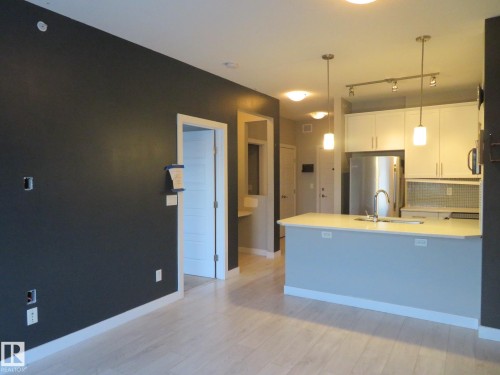 Kitchen with white cabinetry, a peninsula, freestanding refrigerator, tasteful backsplash, and light wood-type flooring - 415 2590 Anderson Way, Edmonton, AB - Indoor Photo Showing Kitchen
