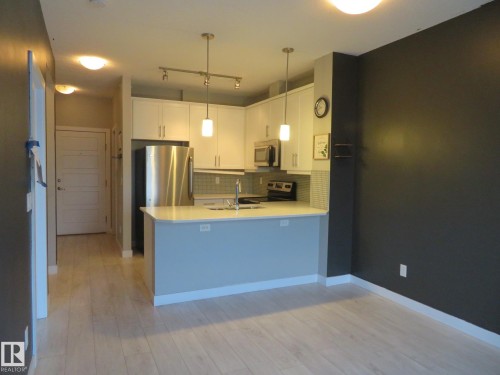 Kitchen featuring light countertops, white cabinetry, stainless steel appliances, a peninsula, and light wood-style flooring - 415 2590 Anderson Way, Edmonton, AB - Indoor Photo Showing Kitchen