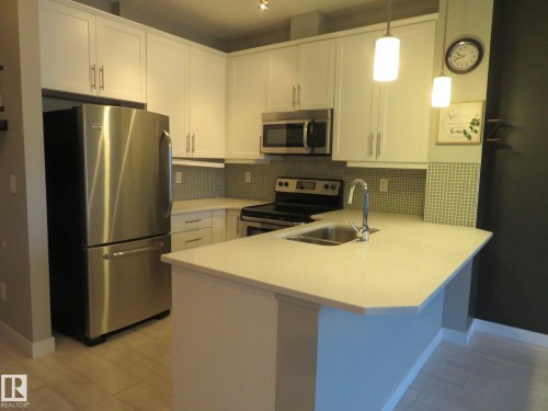 Kitchen featuring stainless steel appliances, a peninsula, white cabinets, light wood-style floors, and hanging light fixtures - 415 2590 Anderson Way, Edmonton, AB - Indoor Photo Showing Kitchen With Double Sink