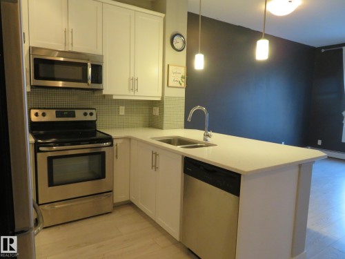 Kitchen featuring stainless steel appliances, white cabinets, light wood-style flooring, a peninsula, and decorative backsplash - 415 2590 Anderson Way, Edmonton, AB - Indoor Photo Showing Kitchen With Double Sink With Upgraded Kitchen