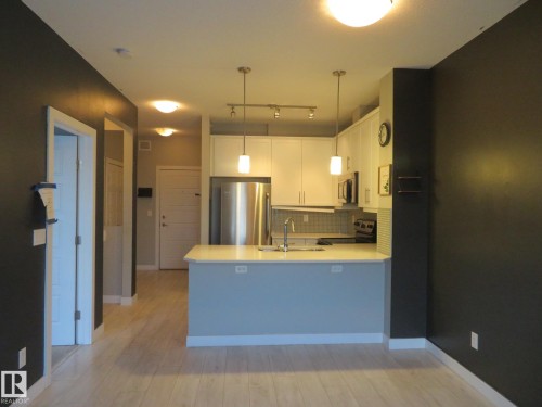 Kitchen featuring white cabinets, stainless steel appliances, a peninsula, light wood-type flooring, and tasteful backsplash - 415 2590 Anderson Way, Edmonton, AB - Indoor Photo Showing Kitchen