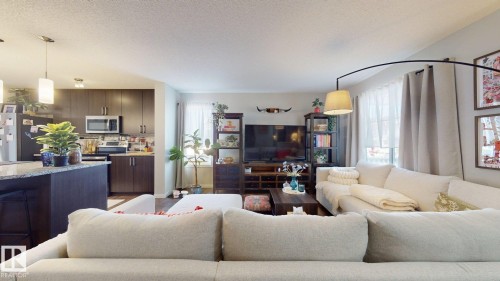 This open-concept living space features hardwood flooring, a kitchen island with pendant lighting, and ample natural light from the windows - 1275 Chappelle Boulevard, Edmonton, AB - Indoor Photo Showing Living Room