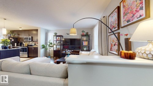 Open concept living area featuring a kitchen with dark cabinetry, stainless steel appliances, and a central island, and a living room with light-colored walls and large windows - 1275 Chappelle Boulevard, Edmonton, AB - Indoor Photo Showing Living Room