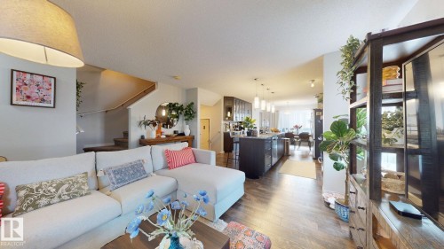 Spacious open-concept living area featuring wood flooring, a staircase with wood banister, and a kitchen with dark cabinetry and pendant lighting - 1275 Chappelle Boulevard, Edmonton, AB - Indoor Photo Showing Other Room