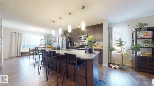 Open-concept living area with dark wood flooring, an extensive kitchen island with a granite countertop, and pendant lighting - 1275 Chappelle Boulevard, Edmonton, AB - Indoor