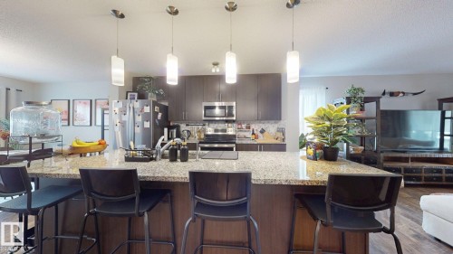 The kitchen features a spacious island with a speckled countertop, a stainless steel refrigerator, and a matching stainless steel oven - 1275 Chappelle Boulevard, Edmonton, AB - Indoor Photo Showing Kitchen With Upgraded Kitchen