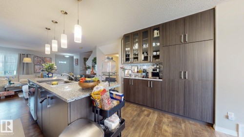 The kitchen features a large island with a sink and granite countertop, pendant lighting, and extensive cabinetry including glass-fronted upper cabinets - 1275 Chappelle Boulevard, Edmonton, AB - Indoor Photo Showing Kitchen With Double Sink