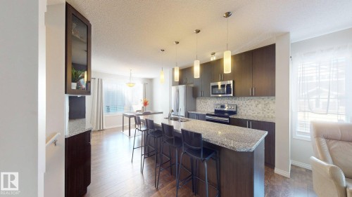 Kitchen with an island with sink, light stone counters, stainless steel appliances, dark wood-style floors, and a kitchen breakfast bar - 1275 Chappelle Boulevard, Edmonton, AB - Indoor Photo Showing Kitchen With Upgraded Kitchen
