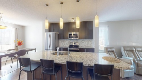 Kitchen featuring a breakfast bar, dark wood finish cabinetry, stainless steel appliances, light stone counters, and dark wood-type flooring - 1275 Chappelle Boulevard, Edmonton, AB - Indoor Photo Showing Kitchen With Double Sink With Upgraded Kitchen