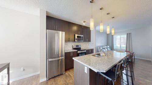 Kitchen featuring dark wood finish cabinetry, stainless steel appliances, a kitchen bar, light stone counters, and an island with sink - 1275 Chappelle Boulevard, Edmonton, AB - Indoor Photo Showing Kitchen With Double Sink With Upgraded Kitchen