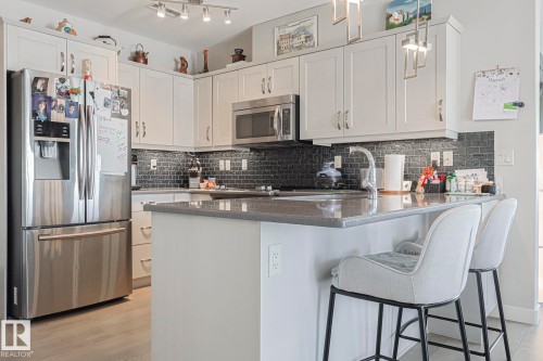 Kitchen with stainless steel appliances, a peninsula, a kitchen bar, white cabinetry, and hanging light fixtures - 910 2755 109 Street, Edmonton, AB - Indoor Photo Showing Kitchen With Stainless Steel Kitchen
