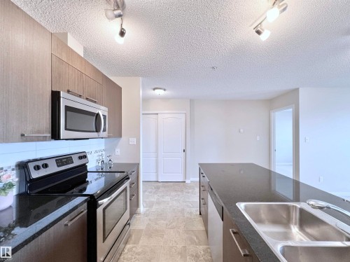 Kitchen with rail lighting, stainless steel appliances, dark stone countertops, a textured ceiling, and modern cabinets - 3308 9351 Simpson Drive, Edmonton, AB - Indoor Photo Showing Kitchen With Double Sink