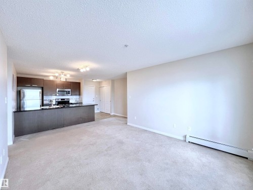 Unfurnished living room with baseboard heating, light colored carpet, and a textured ceiling - 3308 9351 Simpson Drive, Edmonton, AB - Indoor
