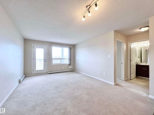 Empty room featuring light carpet, a textured ceiling, baseboard heating, and track lighting - 3308 9351 Simpson Drive, Edmonton, AB - Indoor Photo Showing Other Room