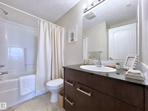 Bathroom featuring vanity, shower / bathtub combination with curtain, a textured ceiling, and light tile patterned floors - 3308 9351 Simpson Drive, Edmonton, AB - Indoor Photo Showing Bathroom