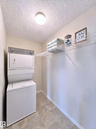 Laundry area with a textured ceiling and stacked washing machine and dryer - 3308 9351 Simpson Drive, Edmonton, AB - Indoor Photo Showing Laundry Room