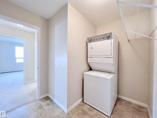 Laundry area with stacked washer and clothes dryer, a textured ceiling, and a baseboard radiator - 3308 9351 Simpson Drive, Edmonton, AB - Indoor Photo Showing Laundry Room