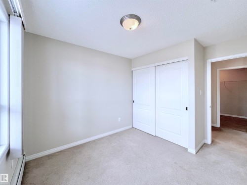 Unfurnished bedroom with a baseboard radiator, light colored carpet, a closet, and a textured ceiling - 3308 9351 Simpson Drive, Edmonton, AB - Indoor Photo Showing Other Room