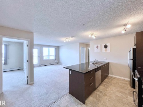 Kitchen with a peninsula, open floor plan, dark wood finish cabinets, stainless steel appliances, and a baseboard heating unit - 3308 9351 Simpson Drive, Edmonton, AB - Indoor Photo Showing Kitchen With Double Sink