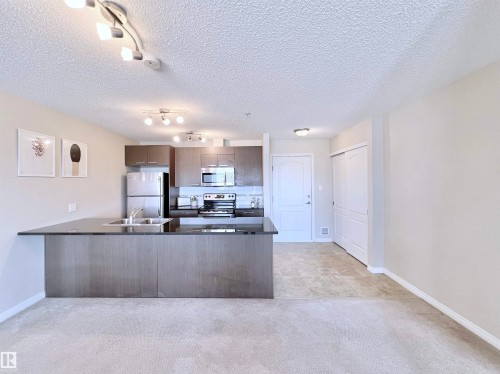 Kitchen featuring a peninsula, dark countertops, stainless steel appliances, track lighting, and a textured ceiling - 3308 9351 Simpson Drive, Edmonton, AB - Indoor Photo Showing Kitchen With Double Sink
