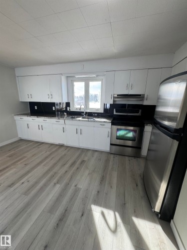 Kitchen with stainless steel appliances, light wood finished floors, dark countertops, and white cabinets - 4801 52 Avenue, Andrew, AB - Indoor Photo Showing Kitchen