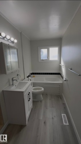 Full bathroom with vanity, light wood-style floors, crown molding, and a bathtub - 4801 52 Avenue, Andrew, AB - Indoor Photo Showing Laundry Room