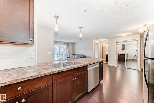 Kitchen featuring stainless steel appliances, decorative light fixtures, a peninsula, open floor plan, and dark wood-type flooring - 229 6076 Schonsee Way, Edmonton, AB - Indoor Photo Showing Kitchen With Stainless Steel Kitchen With Double Sink