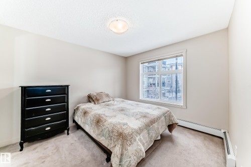 Bedroom with carpet, a baseboard heating unit, and a textured ceiling - 229 6076 Schonsee Way, Edmonton, AB - Indoor Photo Showing Bedroom