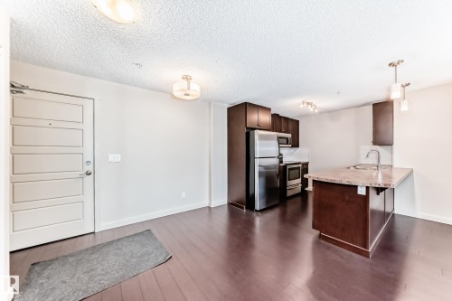Kitchen featuring dark brown cabinets, light countertops, a breakfast bar, a peninsula, and appliances with stainless steel finishes - 229 6076 Schonsee Way, Edmonton, AB - Indoor Photo Showing Kitchen