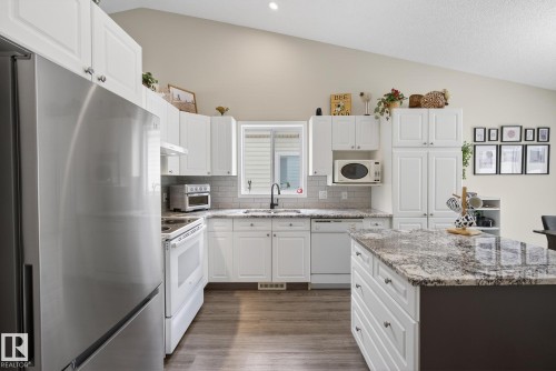 Kitchen with white appliances, light stone countertops, lofted ceiling, white cabinetry, and dark wood finished floors - 30 4 Heritage Way, St. Albert, AB - Indoor Photo Showing Kitchen With Upgraded Kitchen